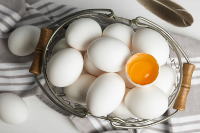 Photo of Many raw chicken eggs in metal basket on white wooden table, flat lay