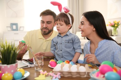 Photo of Happy family painting Easter eggs at table indoors