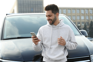 Photo of Handsome young man with smartphone near modern car outdoors