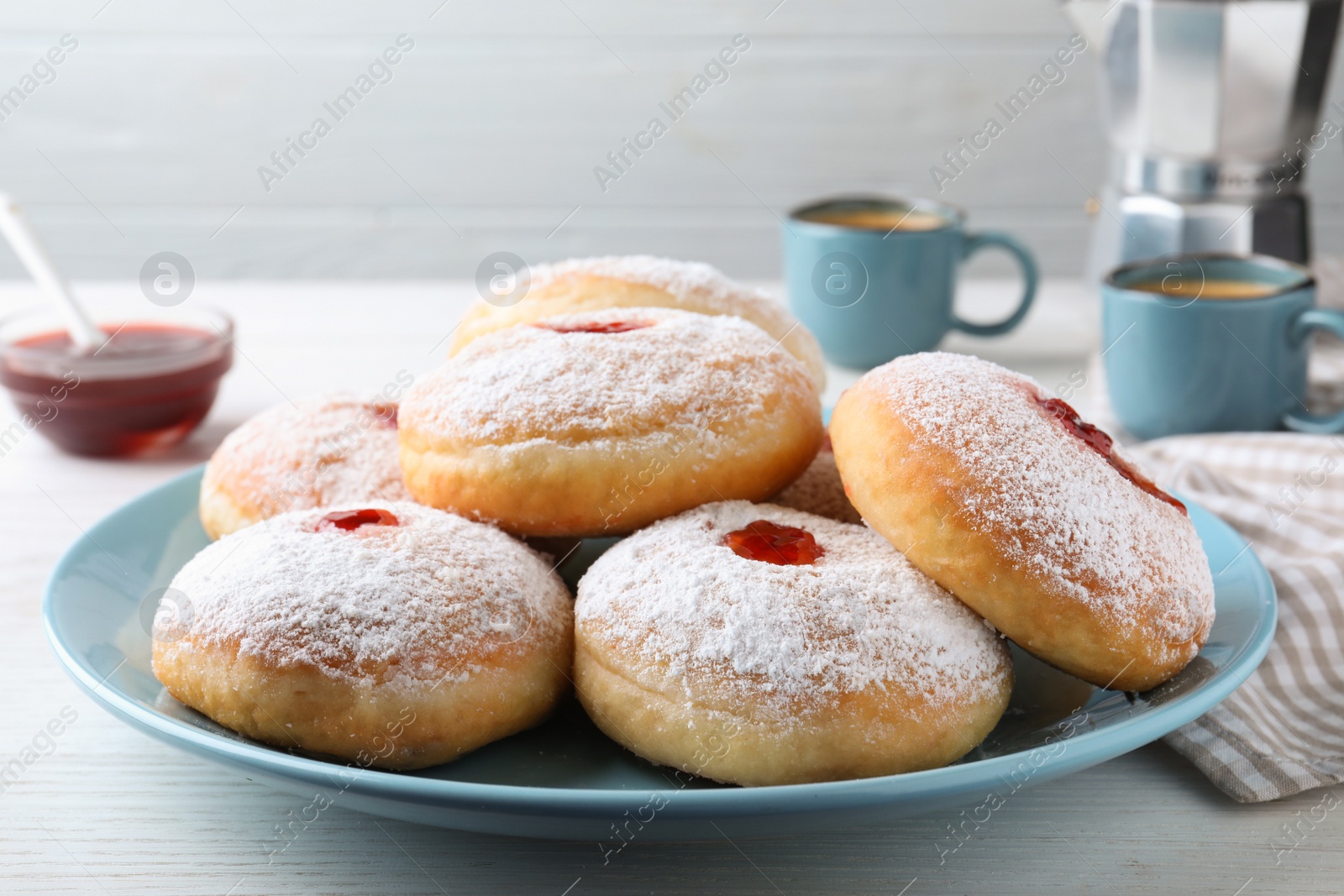 Photo of Delicious donuts with jam and powdered sugar on white table, closeup