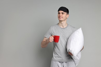 Photo of Man in pyjama holding pillow and cup of drink on grey background, space for text