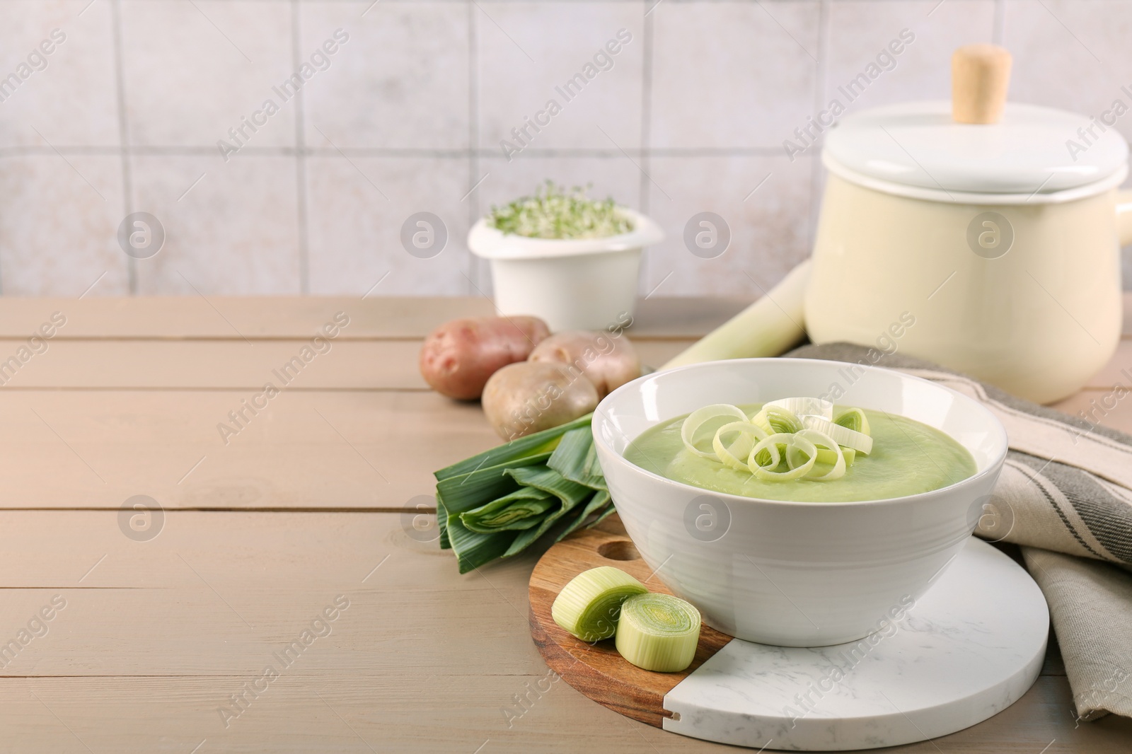 Photo of Tasty leek soup in bowl and fresh ingredients on wooden table, space for text