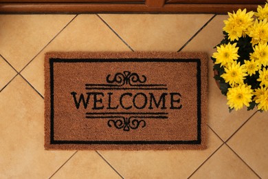 Photo of Door mat with word Welcome and beautiful flowers on floor, flat lay