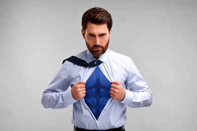 Confident businessman wearing superhero costume under suit on light grey background