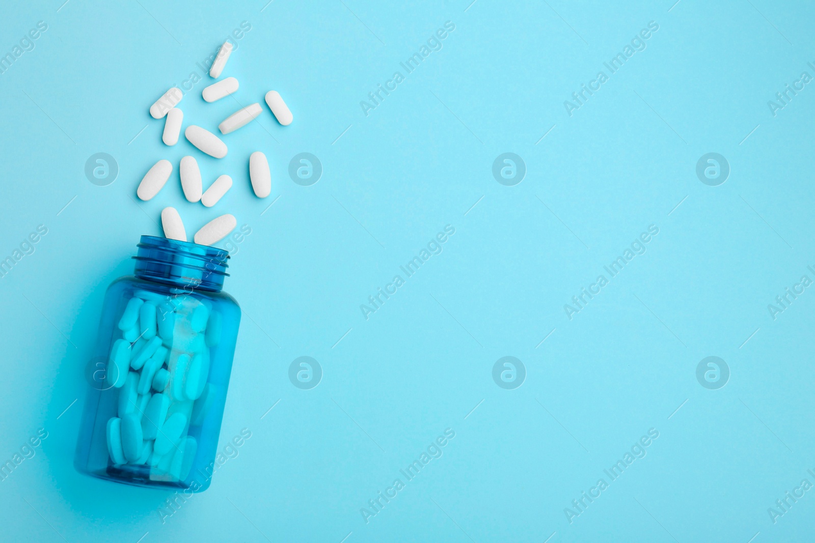 Photo of Vitamin pills and bottle on light blue background, top view. Space for text