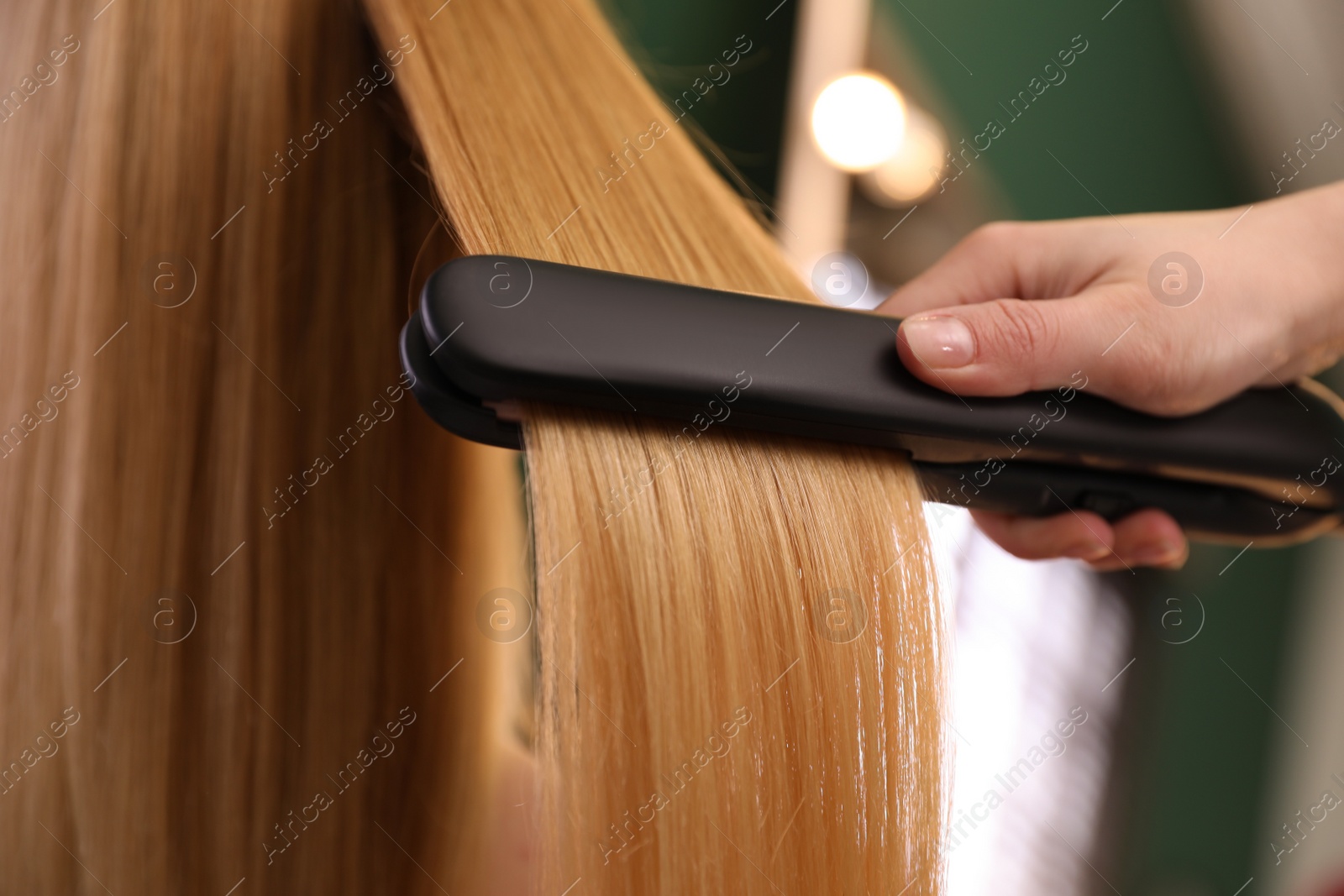 Photo of Stylist straightening woman's hair with flat iron in salon, closeup