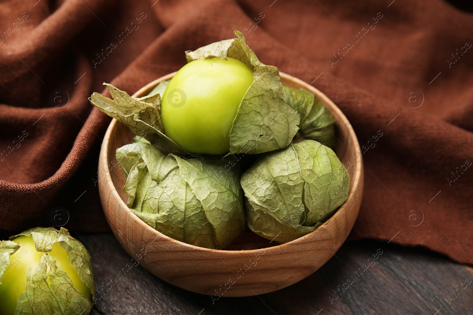 Photo of Fresh green tomatillos with husk in bowl on wooden table, closeup