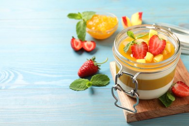 Photo of Delicious panna cotta with mango coulis and fresh fruits on light blue wooden table. Space for text
