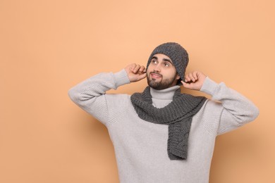 Smiling man in knitted scarf and hat on beige background. Space for text