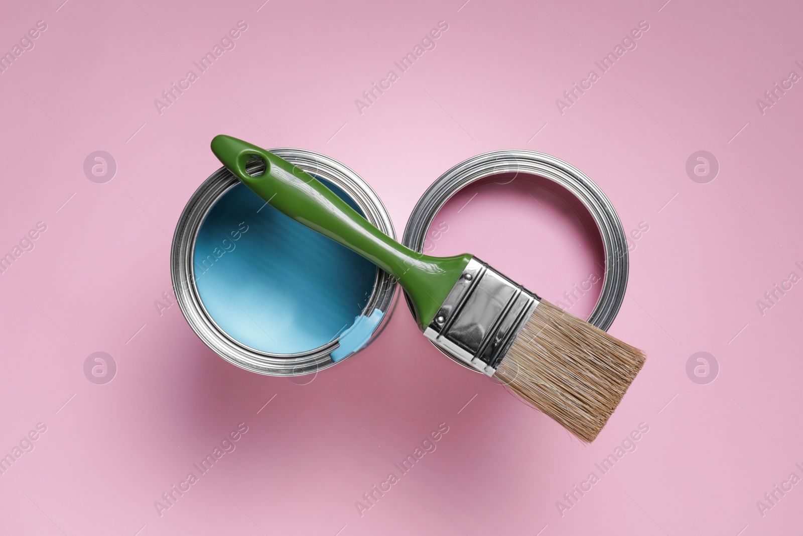 Photo of Cans with different paints and brush on pink background, flat lay