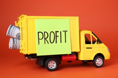 Photo of Economic profit concept. Toy truck with banknotes on red background