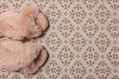Fluffy beige slippers on carpet, top view. Space for text