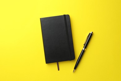 Photo of Closed black notebook and pen on yellow background, top view