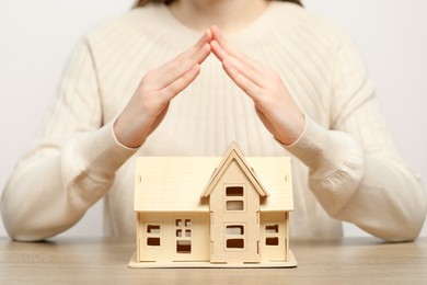 Photo of Home security concept. Woman covering house model at wooden table, closeup