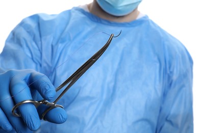 Photo of Doctor holding forceps with suture thread on white background, closeup. Medical equipment