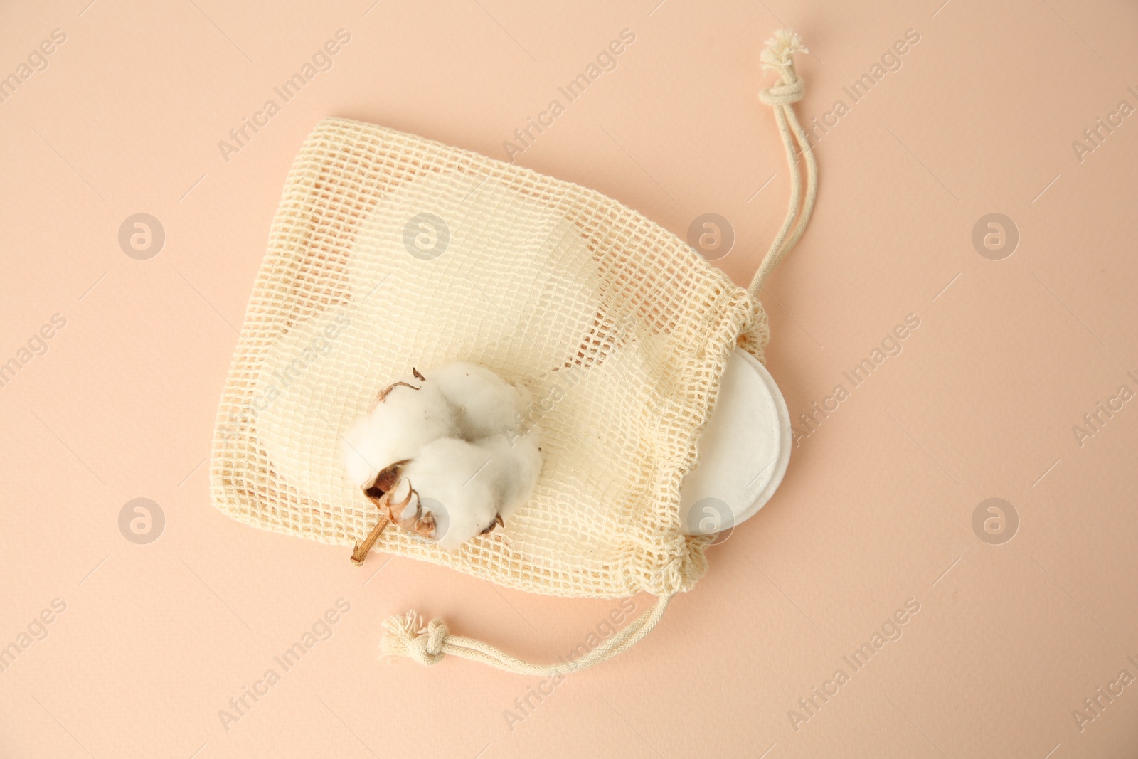 Photo of Bag with cotton pads and flower on beige background, flat lay