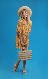 Photo of Young woman wearing stylish dress with straw bag on blue background