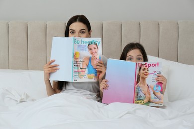 Photo of Young mother and her daughter with magazines on bed at home