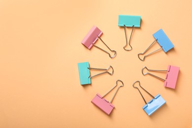 Colorful binder clips on beige background, flat lay. Space for text