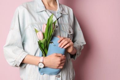 Photo of Stylish woman with bag and spring flowers against color background, closeup