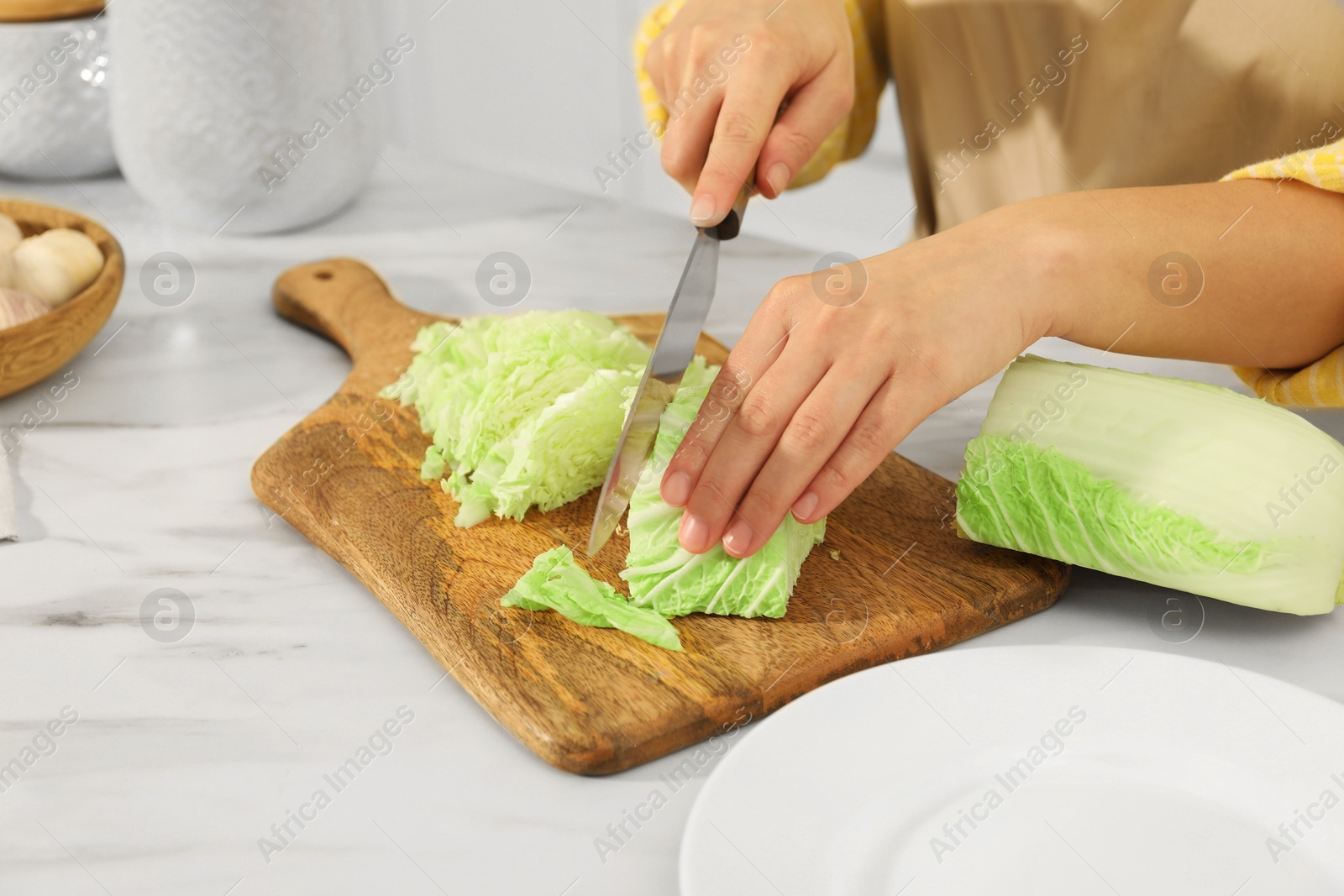 Photo of Woman cutting fresh chinese cabbage at table in kitchen, closeup