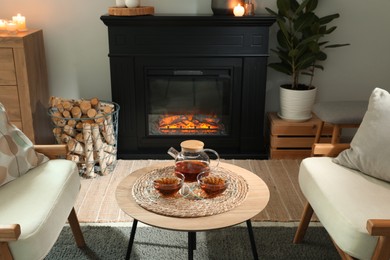 Photo of Stylish fireplace near comfortable armchairs and coffee table with tea in cosy living room. Interior design