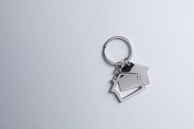 Metallic keychains in shape of houses on light grey background, top view. Space for text