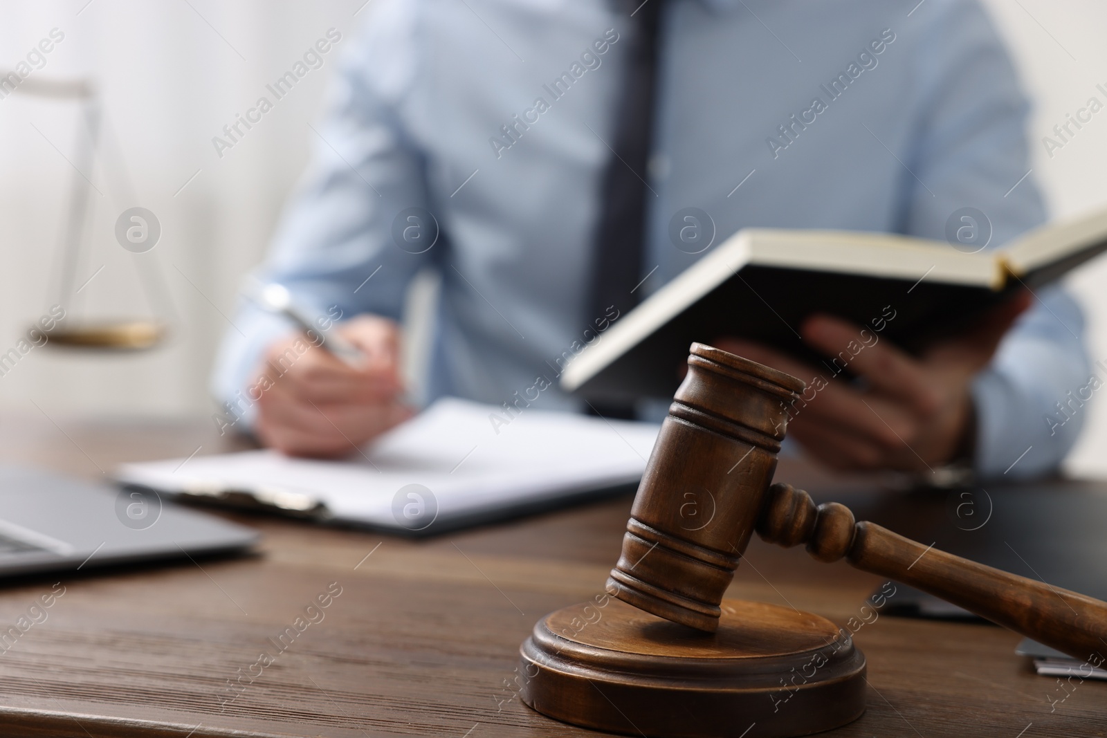 Photo of Lawyer working at wooden table indoors, focus on gavel