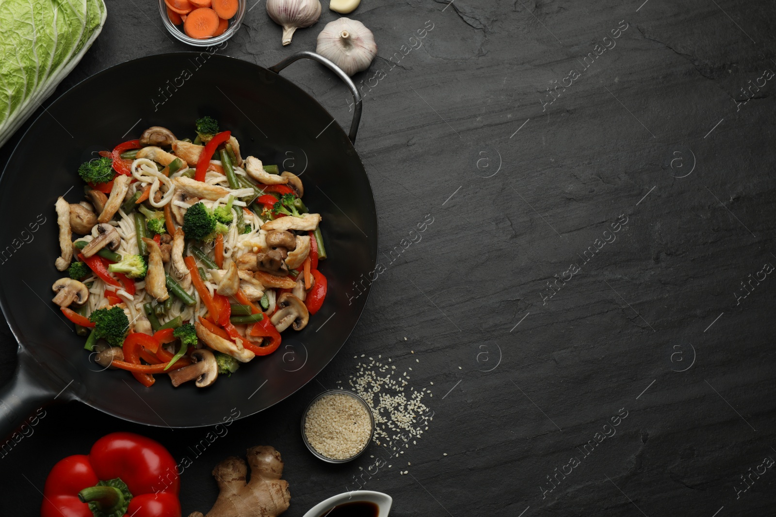 Photo of Stir fried noodles with mushrooms, chicken and vegetables in wok on black table, flat lay. Space for text