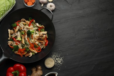 Stir fried noodles with mushrooms, chicken and vegetables in wok on black table, flat lay. Space for text
