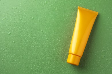 Photo of Moisturizing cream in tube on green background with water drops, top view. Space for text