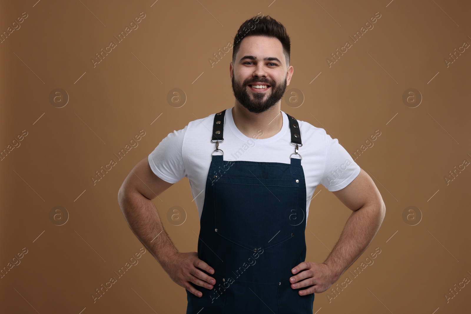 Photo of Smiling man in kitchen apron on brown background. Mockup for design