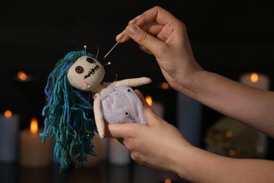 Woman stabbing voodoo doll with pin in dark room, closeup. Curse ceremony