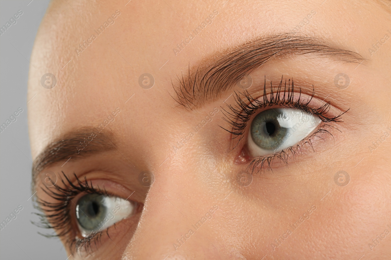 Photo of Woman with long eyelashes after mascara applying against grey background, closeup