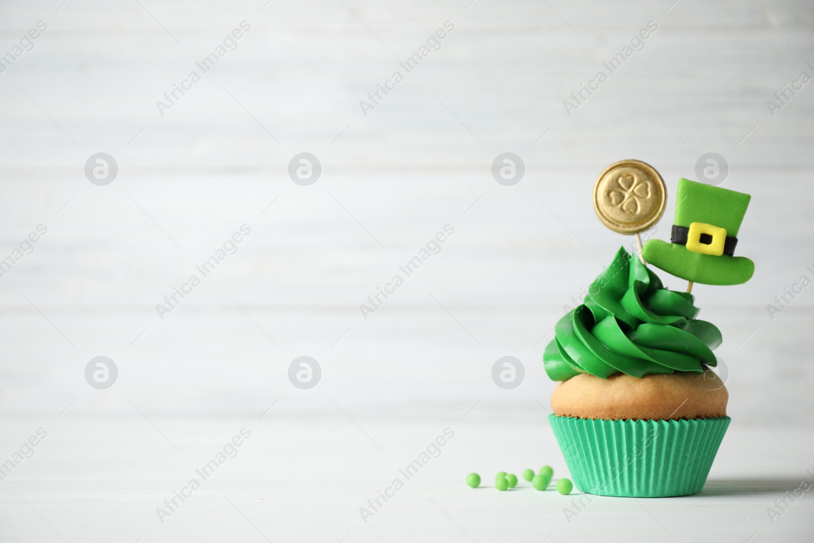 Photo of Decorated cupcake on white wooden table, space for text. St. Patrick's Day celebration