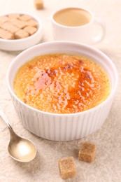 Delicious creme brulee in bowl, sugar cubes, coffee and spoon on light textured table, closeup