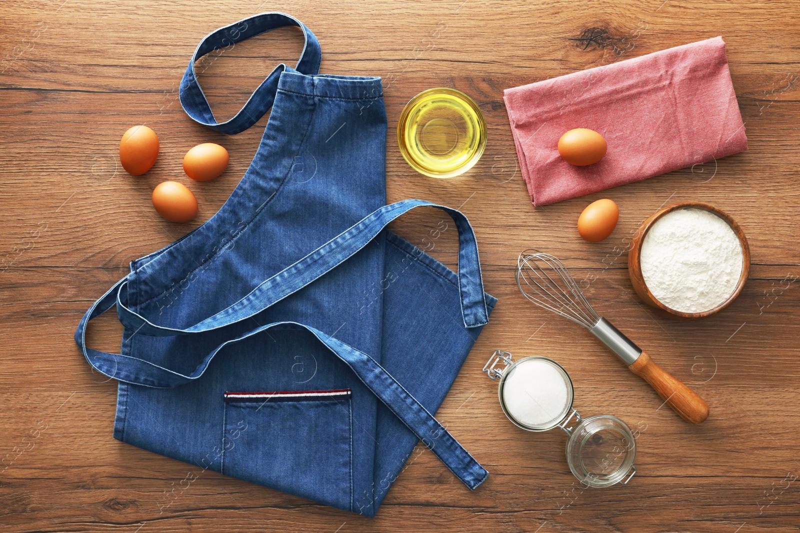 Photo of Denim apron with kitchen tool and different ingredients on wooden table, flat lay