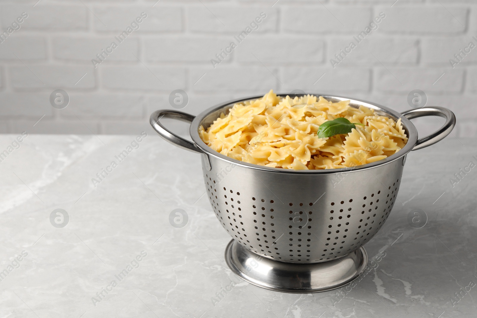 Photo of Cooked pasta in metal colander on grey marble table. Space for text