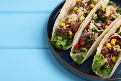 Delicious tacos with meat and vegetables on light blue table, closeup. Space for text