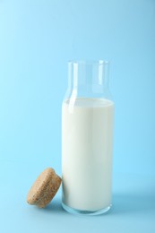 Glass carafe of fresh milk and lid on light blue background