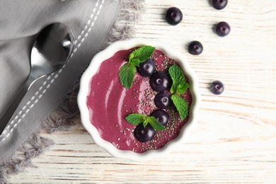 Photo of Flat lay composition with bowl of tasty acai smoothie on wooden table