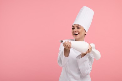 Photo of Happy professional confectioner in uniform holding piping bag on pink background. Space for text