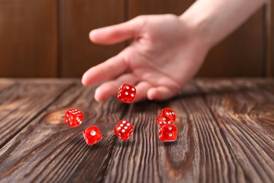 Image of Woman throwing red dice on wooden table, closeup
