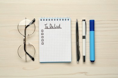 Notepad with unfilled To Do list, stationery and glasses on wooden table, flat lay
