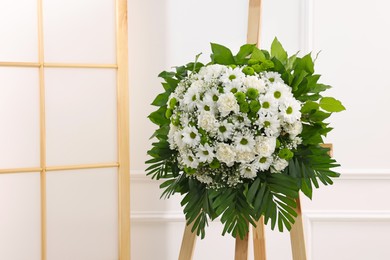 Photo of Funeral wreath of flowers on wooden stand near white wall