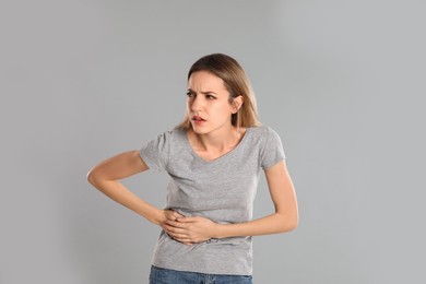 Young woman suffering from liver pain on grey background