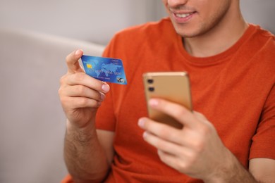 Man using smartphone and credit card for online payment at home, closeup