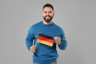 Young man holding flag of Germany on light grey background