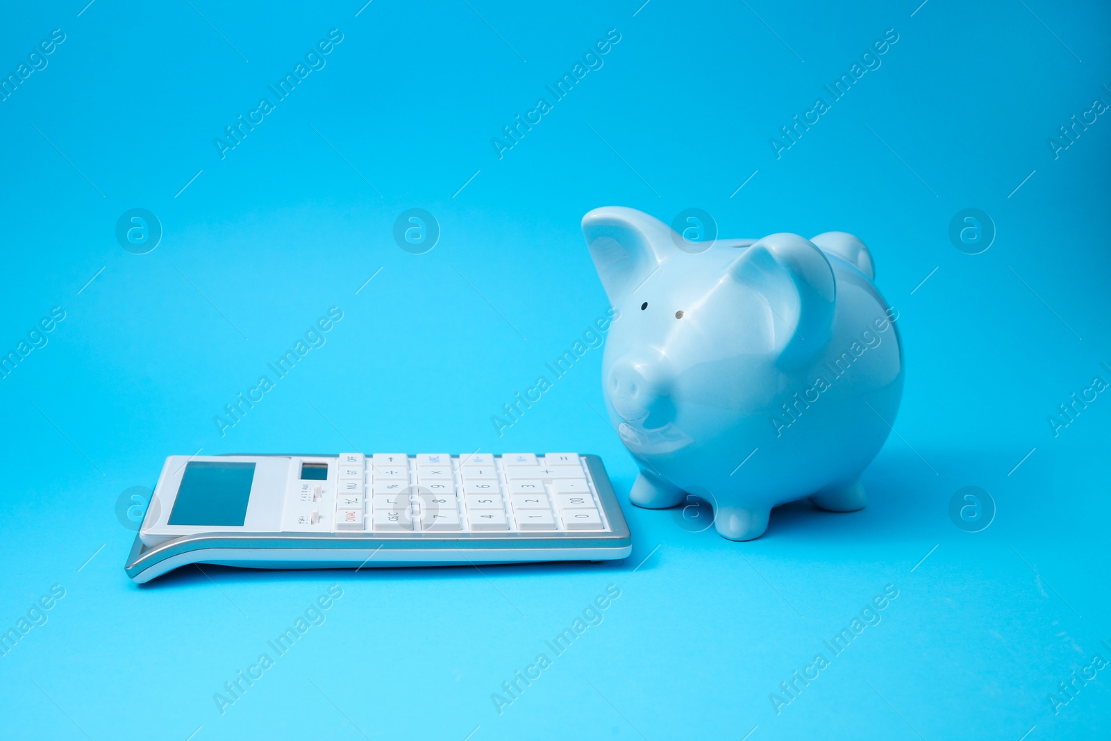 Photo of Piggy bank and calculator on light blue background