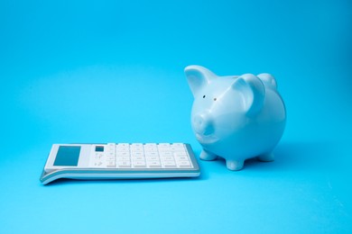 Photo of Piggy bank and calculator on light blue background